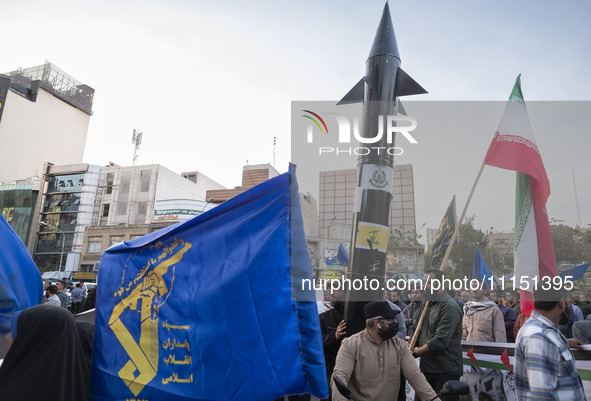 Veiled women are waving an Iranian flag and a flag of the Islamic Revolutionary Guard Corps while two unidentified men are carrying a model...