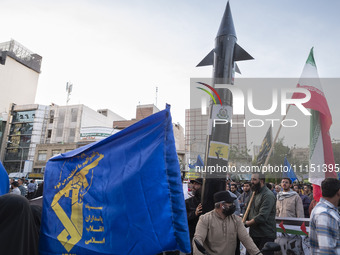 Veiled women are waving an Iranian flag and a flag of the Islamic Revolutionary Guard Corps while two unidentified men are carrying a model...