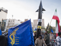 Veiled women are waving an Iranian flag and a flag of the Islamic Revolutionary Guard Corps while two unidentified men are carrying a model...