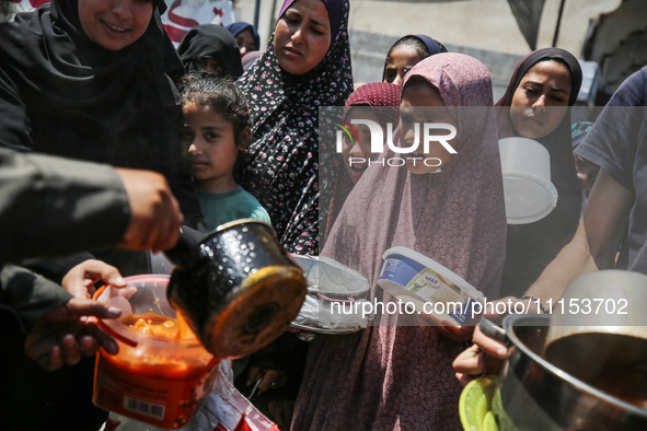 Displaced Palestinians are receiving cooked food rations at a donation point in Deir al-Balah in the central Gaza Strip, on April 16, 2024,...