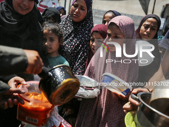 Displaced Palestinians are receiving cooked food rations at a donation point in Deir al-Balah in the central Gaza Strip, on April 16, 2024,...