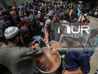 Displaced Palestinians are receiving cooked food rations at a donation point in Deir al-Balah in the central Gaza Strip, on April 16, 2024,...