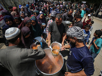 Displaced Palestinians are receiving cooked food rations at a donation point in Deir al-Balah in the central Gaza Strip, on April 16, 2024,...