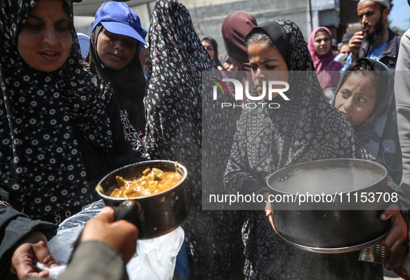 Displaced Palestinians are receiving cooked food rations at a donation point in Deir al-Balah in the central Gaza Strip, on April 16, 2024,...