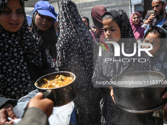 Displaced Palestinians are receiving cooked food rations at a donation point in Deir al-Balah in the central Gaza Strip, on April 16, 2024,...