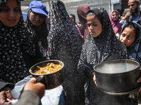 Displaced Palestinians are receiving cooked food rations at a donation point in Deir al-Balah in the central Gaza Strip, on April 16, 2024,...