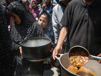 Displaced Palestinians are receiving cooked food rations at a donation point in Deir al-Balah in the central Gaza Strip, on April 16, 2024,...