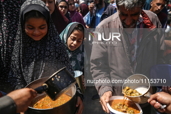 Displaced Palestinians are receiving cooked food rations at a donation point in Deir al-Balah in the central Gaza Strip, on April 16, 2024,...