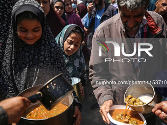 Displaced Palestinians are receiving cooked food rations at a donation point in Deir al-Balah in the central Gaza Strip, on April 16, 2024,...