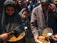 Displaced Palestinians are receiving cooked food rations at a donation point in Deir al-Balah in the central Gaza Strip, on April 16, 2024,...