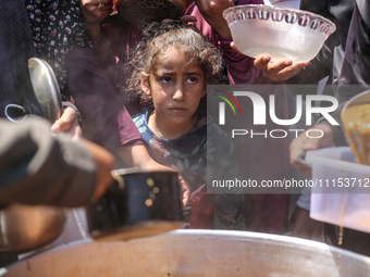 Displaced Palestinians are receiving cooked food rations at a donation point in Deir al-Balah in the central Gaza Strip, on April 16, 2024,...