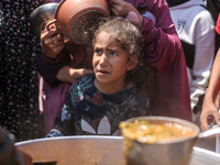 Displaced Palestinians are receiving cooked food rations at a donation point in Deir al-Balah in the central Gaza Strip, on April 16, 2024,...