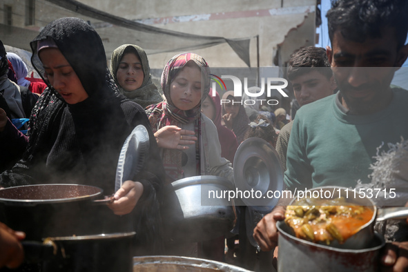 Displaced Palestinians are receiving cooked food rations at a donation point in Deir al-Balah in the central Gaza Strip, on April 16, 2024,...