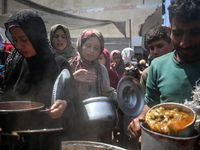 Displaced Palestinians are receiving cooked food rations at a donation point in Deir al-Balah in the central Gaza Strip, on April 16, 2024,...