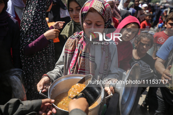 Displaced Palestinians are receiving cooked food rations at a donation point in Deir al-Balah in the central Gaza Strip, on April 16, 2024,...