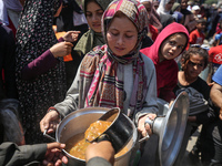 Displaced Palestinians are receiving cooked food rations at a donation point in Deir al-Balah in the central Gaza Strip, on April 16, 2024,...