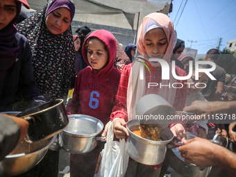 Displaced Palestinians are receiving cooked food rations at a donation point in Deir al-Balah in the central Gaza Strip, on April 16, 2024,...