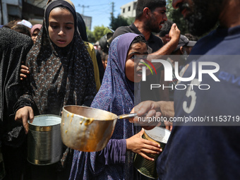 Displaced Palestinians are receiving cooked food rations at a donation point in Deir al-Balah in the central Gaza Strip, on April 16, 2024,...