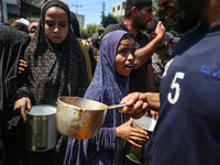 Displaced Palestinians are receiving cooked food rations at a donation point in Deir al-Balah in the central Gaza Strip, on April 16, 2024,...