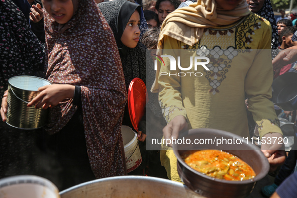 Displaced Palestinians are receiving cooked food rations at a donation point in Deir al-Balah in the central Gaza Strip, on April 16, 2024,...