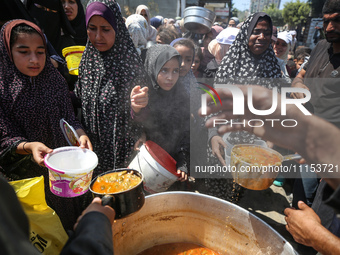 Displaced Palestinians are receiving cooked food rations at a donation point in Deir al-Balah in the central Gaza Strip, on April 16, 2024,...