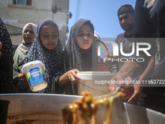 Displaced Palestinians are receiving cooked food rations at a donation point in Deir al-Balah in the central Gaza Strip, on April 16, 2024,...