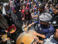 Displaced Palestinians are receiving cooked food rations at a donation point in Deir al-Balah in the central Gaza Strip, on April 16, 2024,...