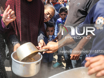 Displaced Palestinians are receiving cooked food rations at a donation point in Deir al-Balah in the central Gaza Strip, on April 16, 2024,...