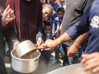 Displaced Palestinians are receiving cooked food rations at a donation point in Deir al-Balah in the central Gaza Strip, on April 16, 2024,...