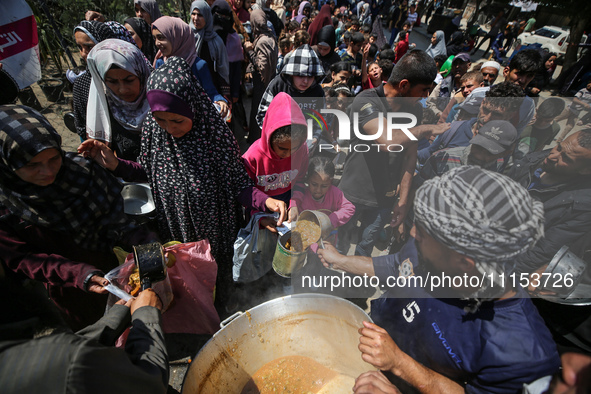 Displaced Palestinians are receiving cooked food rations at a donation point in Deir al-Balah in the central Gaza Strip, on April 16, 2024,...