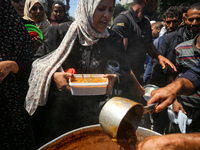 Displaced Palestinians are receiving cooked food rations at a donation point in Deir al-Balah in the central Gaza Strip, on April 16, 2024,...