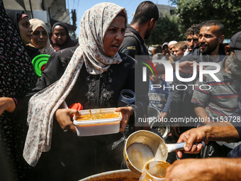 Displaced Palestinians are receiving cooked food rations at a donation point in Deir al-Balah in the central Gaza Strip, on April 16, 2024,...