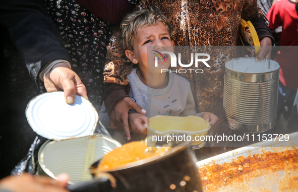 Displaced Palestinians are receiving cooked food rations at a donation point in Deir al-Balah in the central Gaza Strip, on April 16, 2024,...