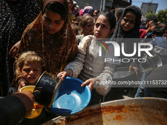 Displaced Palestinians are receiving cooked food rations at a donation point in Deir al-Balah in the central Gaza Strip, on April 16, 2024,...