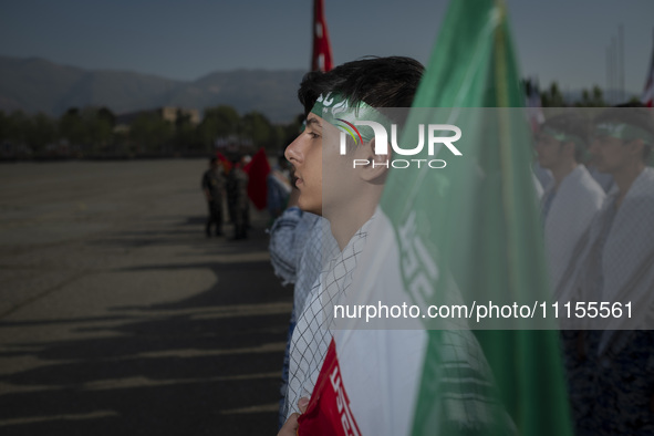 An Iranian schoolboy, who is also a member of the Basij paramilitary force, is standing at attention next to an Iranian flag as he prepares...