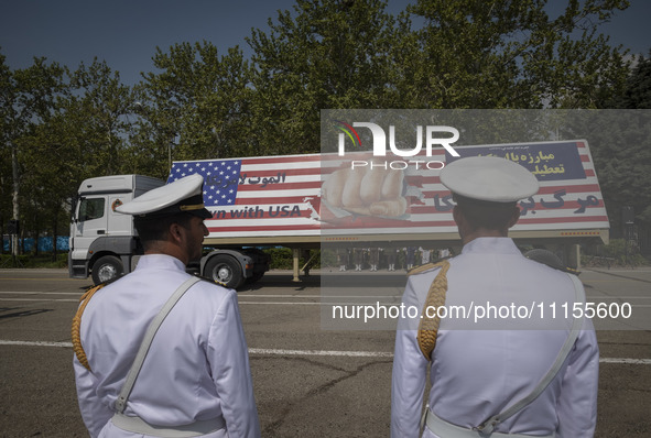 Two members of the Iranian navy are standing at attention as a truck carries a massive anti-U.S. billboard during a military parade marking...