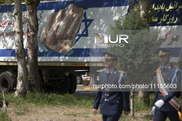 Two members of the Iranian Army's air force are walking past a massive anti-Israeli billboard after a military parade marking the anniversar...