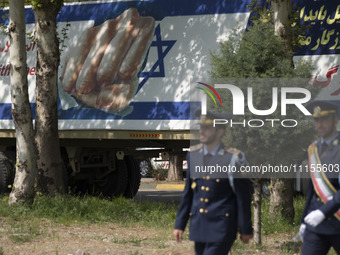 Two members of the Iranian Army's air force are walking past a massive anti-Israeli billboard after a military parade marking the anniversar...