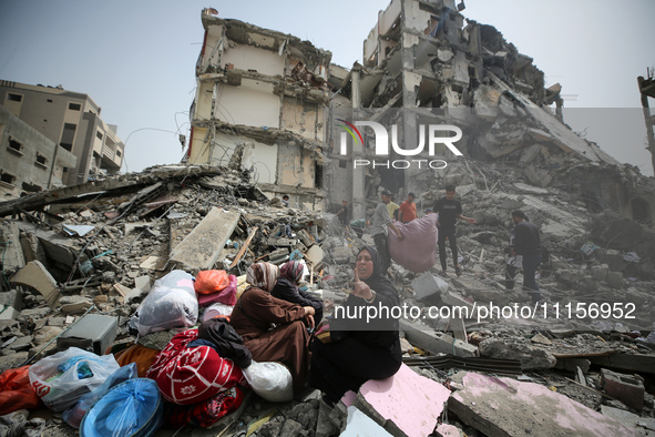 Palestinian women are reacting as they sit on the rubble of a residential building that housed their apartments, following an Israeli raid,...