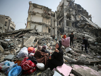 Palestinian women are reacting as they sit on the rubble of a residential building that housed their apartments, following an Israeli raid,...