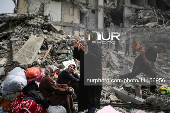 Palestinian women are reacting as they sit on the rubble of a residential building that housed their apartments, following an Israeli raid,...