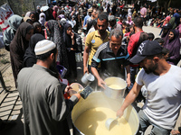 Displaced Palestinians are receiving cooked food rations at a donation point in Deir al-Balah in the central Gaza Strip, on April 19, 2024,...