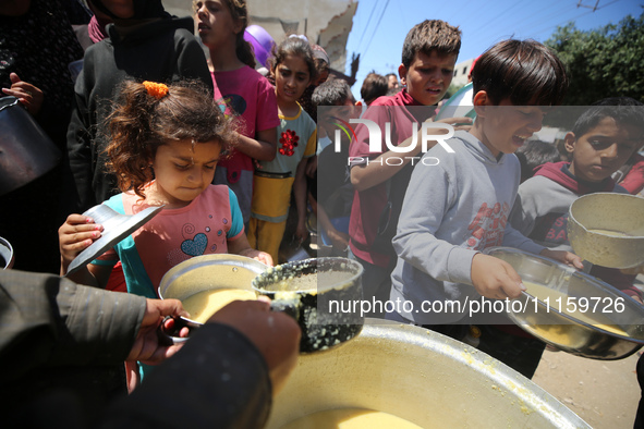 Displaced Palestinians are receiving cooked food rations at a donation point in Deir al-Balah in the central Gaza Strip, on April 19, 2024,...