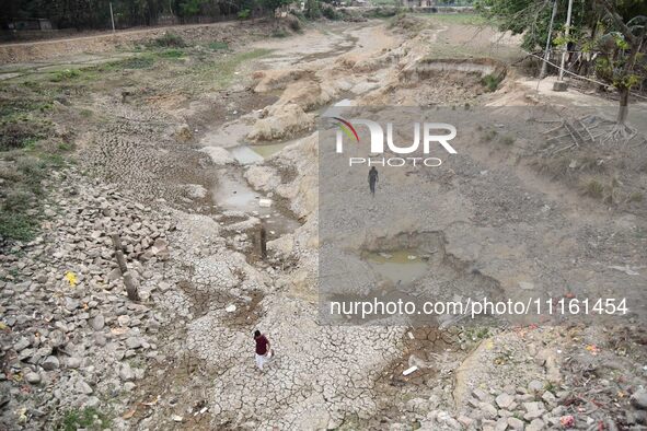 People are walking across the dry bed of a lake in Kathiatoli town, Nagaon District, Assam, India, on April 20, 2024. 