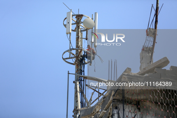 A Palestinian communications engineer is repairing a transmission pole above a destroyed house in the city of Nuseirat in the central Gaza S...