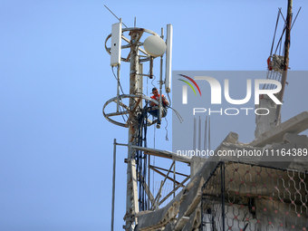 A Palestinian communications engineer is repairing a transmission pole above a destroyed house in the city of Nuseirat in the central Gaza S...