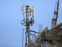 A Palestinian communications engineer is repairing a transmission pole above a destroyed house in the city of Nuseirat in the central Gaza S...