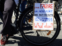 Cyclists are displaying a placard that reads 'For Fabre, an airport, a highway, devastated lands, what else?' as thousands of people are dem...