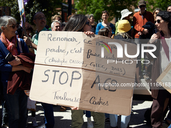 Protesters are holding placards, one of which reads 'to renounce isn't to lose, it's doing differently. Christophe Cassou. IPCC. Stop A69',...