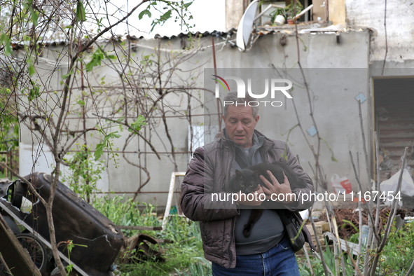 A man is carrying a black cat across a yard in a residential area affected by falling Russian missile debris in the Odesa region, southern U...